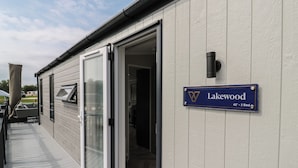 A building with a sliding glass door entrance, a sign indicating 'Lakewood 42' - 2 Bed', and a small outdoor seating area.