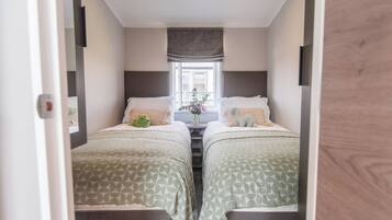 A narrow room with two beds, a window with curtains, and a small table with a vase of flowers.