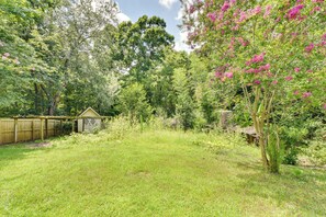 A backyard with a wooden fence, a small shed, and a variety of trees and shrubs. - Matthews Family Home w/ Fenced Yard! (Matthews)