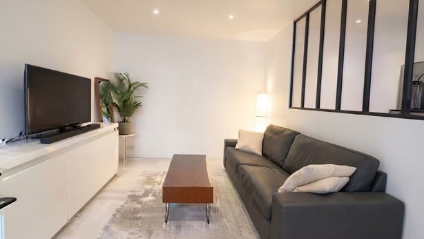 Ett modernt vardagsrum med en platt-TV, en soffa, ett soffbord och ett stort fönster.