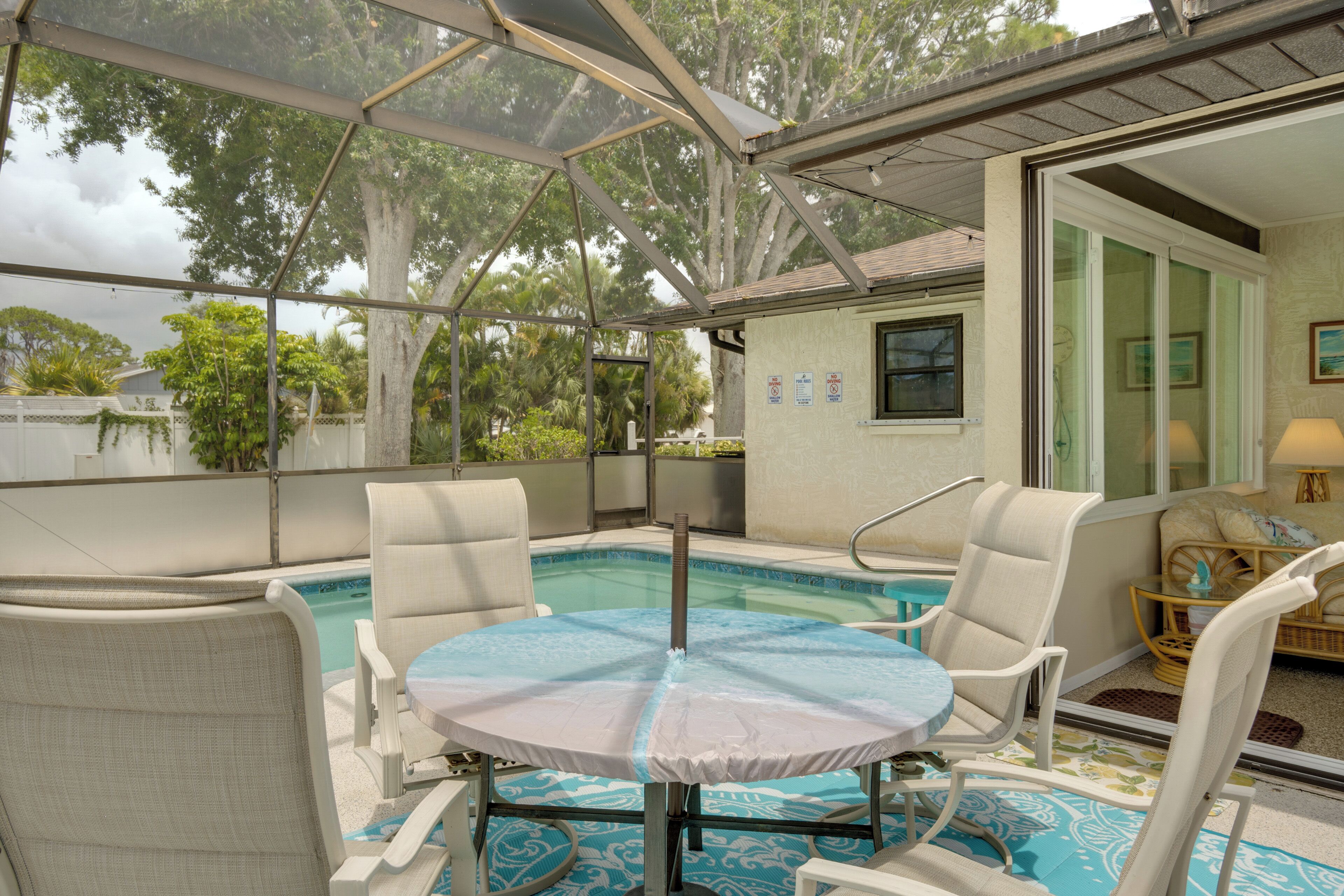 A covered outdoor pool area with chairs and a table, surrounded by a glass enclosure.