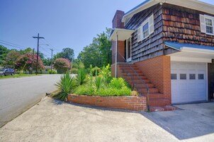 Una casa de dos pisos con cimientos de ladrillo y revestimiento de madera, un jardín delantero con diversas plantas y un garaje.