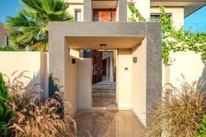 A modern building entrance with a concrete archway, a staircase leading inside, and surrounding greenery. - Villa Vamo | Luxury 5-Bedroom Golf Villa with Heated Pool | Amelkis Marrakech (Marrakech)