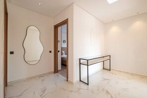 A hallway with a marble floor, a wall-mounted mirror, and a wooden door leading to a bedroom. - Villa Vamo | Luxury 5-Bedroom Golf Villa with Heated Pool | Amelkis Marrakech (Marrakech)