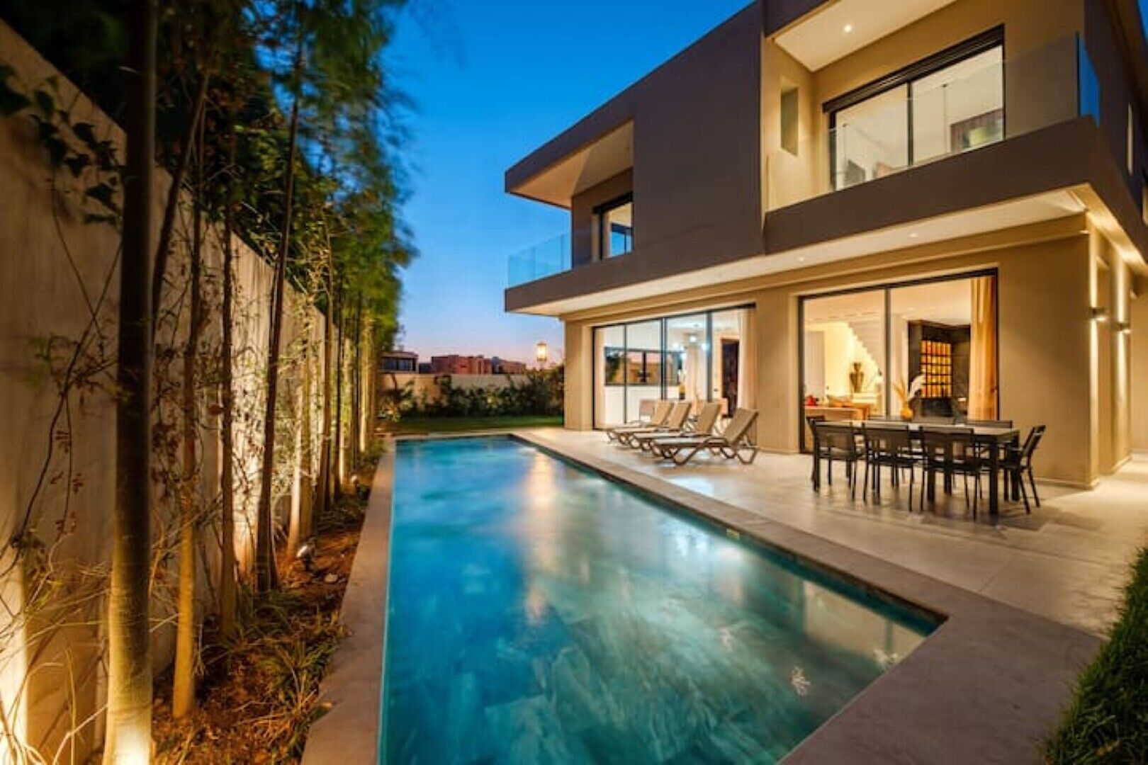 A modern two-story house with a swimming pool, outdoor seating, and a view of the cityscape.