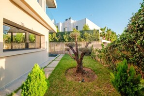 A modern residential area with a well-maintained lawn, a tree, and a fence. - Villa Vamo | Luxury 5-Bedroom Golf Villa with Heated Pool | Amelkis Marrakech (Marrakech)