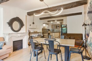 Un coin repas avec une table et des chaises en bois, une cheminée et une cuisine en arrière-plan.