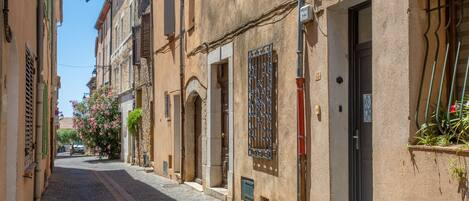 A narrow cobblestone street lined with traditional buildings, featuring arched doorways and wrought iron window grilles.