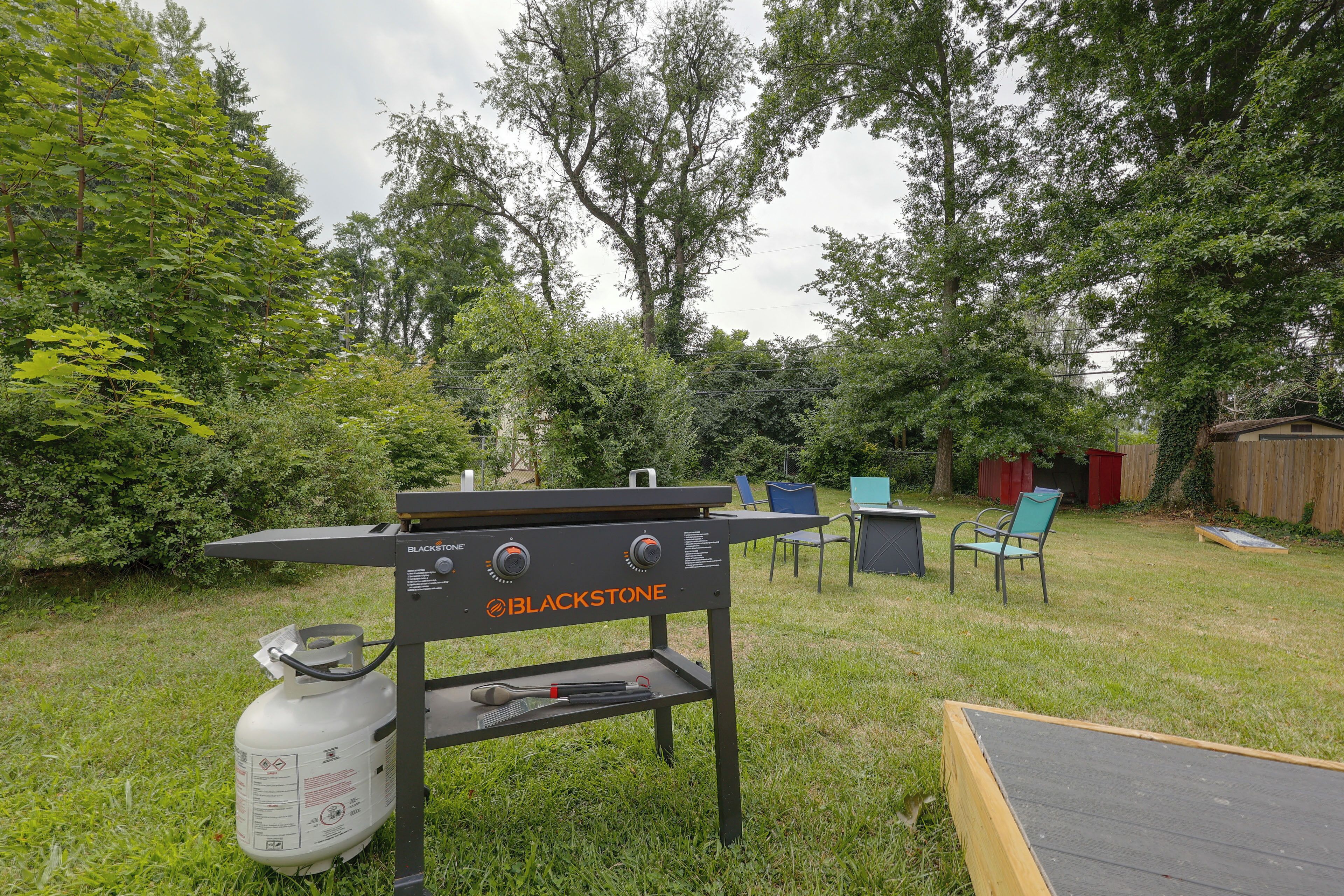 A backyard with a barbecue grill, chairs, and a wooden deck.