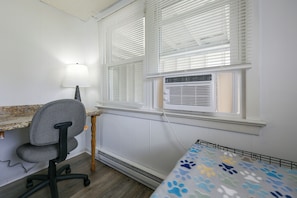 Een kamer met een bureau, stoel, bed en raam met zonwering.