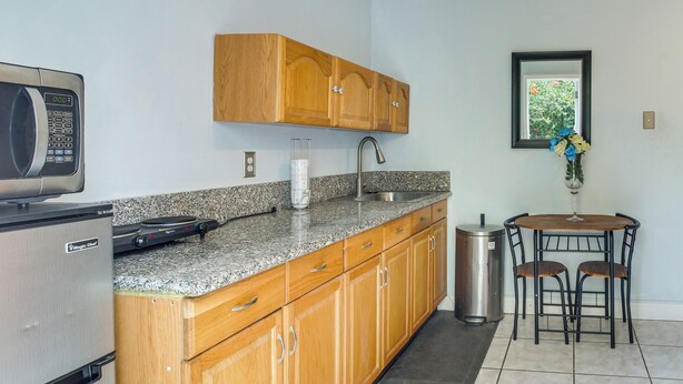 A kitchen with wooden cabinets, a granite countertop, a stainless steel sink, a microwave, and a trash can. - Gateway to Everglades! Extended Stay for Couples (Miami)