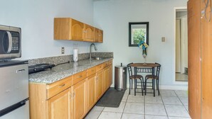 A compact kitchen with wooden cabinets, a granite countertop, a microwave, a sink, and a dining area with a table and chairs. - Gateway to Everglades! Extended Stay for Couples (Miami)