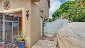 A covered outdoor area with a metal gate, a potted plant, and a car covered with a beige tarp. - Gateway to Everglades! Extended Stay for Couples (Miami)