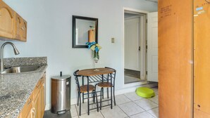 A kitchen with a granite countertop, stainless steel sink, and a trash can. There is a small wooden table with two chairs and a vase with flowers on the wall. - Gateway to Everglades! Extended Stay for Couples (Miami)