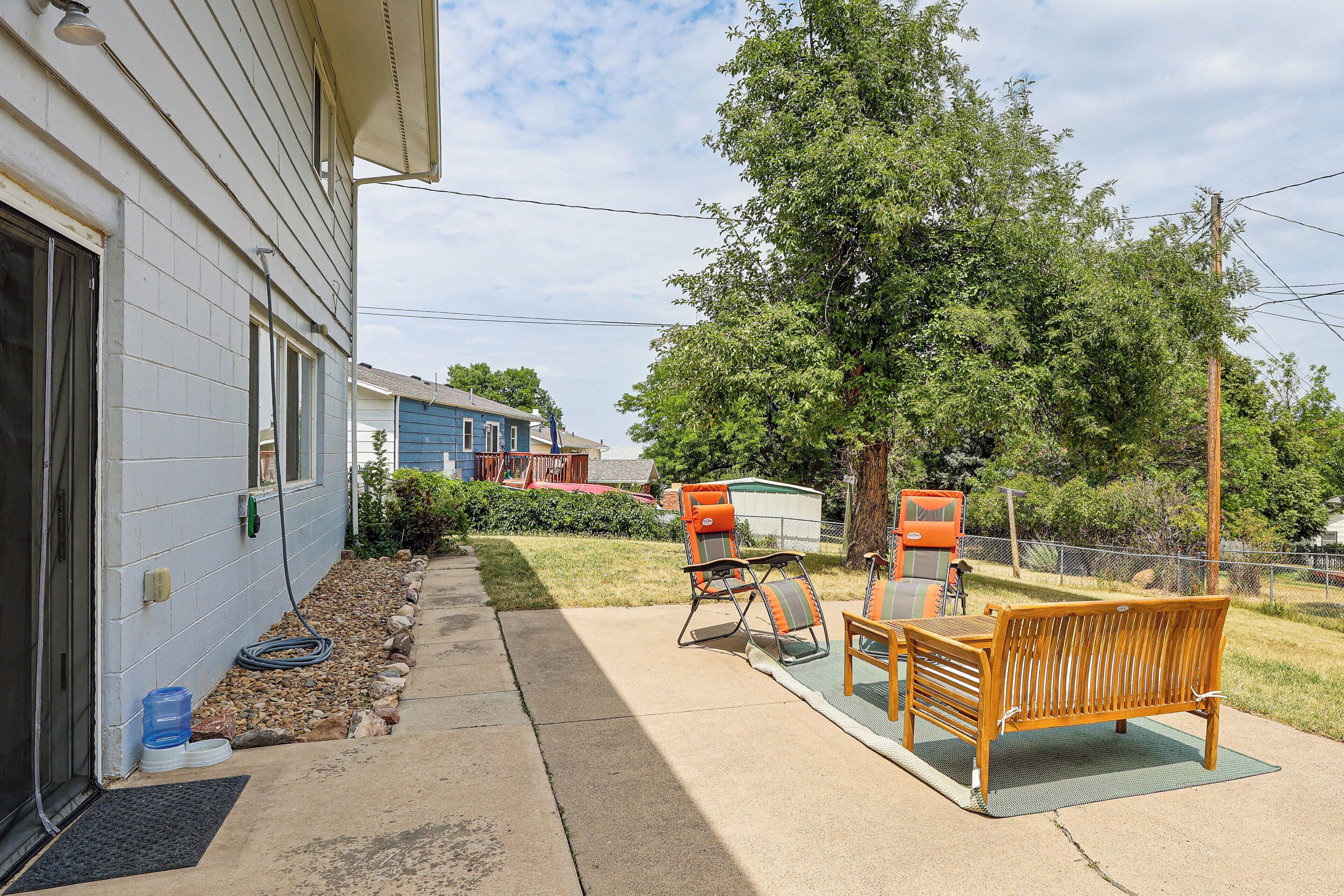 A residential backyard with a patio area, outdoor furniture, and a large tree.