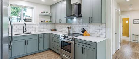 A modern kitchen with grey cabinets, a stainless steel refrigerator, and a built-in oven.