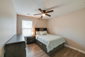 A bedroom with a bed, nightstands, a dresser, a ceiling fan, and a window with blinds.