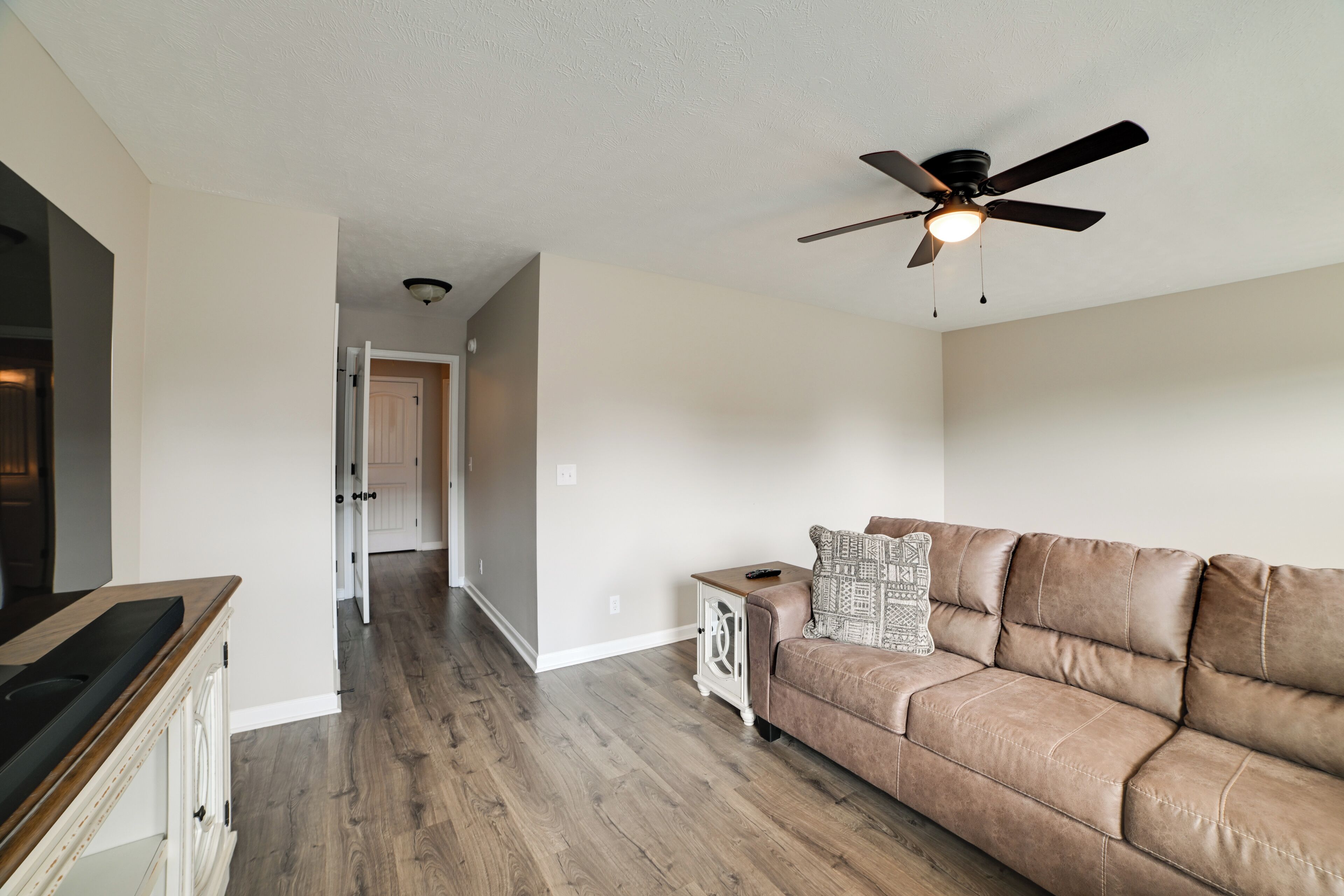 A living room with a brown leather sofa, a ceiling fan, and a wooden cabinet.