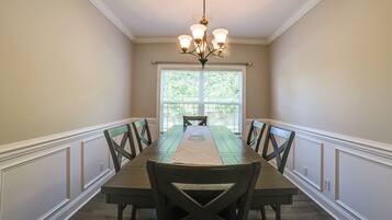 A dining room with a long table, chairs, a chandelier, and a window with blinds.