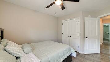 A bedroom with a bed, a ceiling fan, and a door leading to another room.