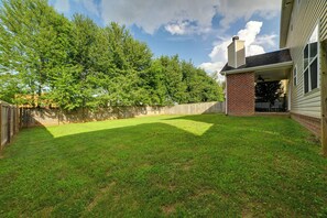 A backyard with a grassy lawn, a wooden fence, and a brick patio area.