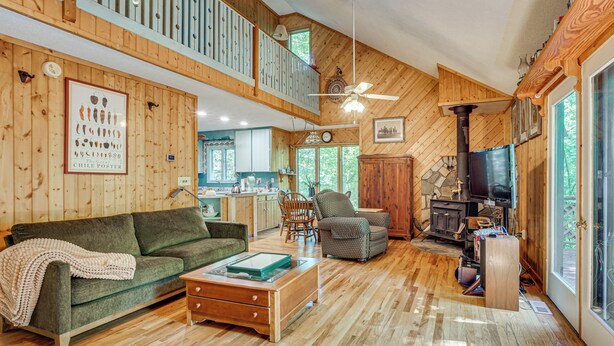 A spacious living area with a high ceiling, wooden floors, a green sofa, a patterned armchair, a wooden coffee table, and a fireplace. - 9 Mi to Lake Keowee! Secluded Creekfront Getaway (Sunset)