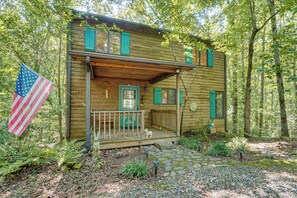 A wooden cabin with a porch, a small dog, and an American flag.