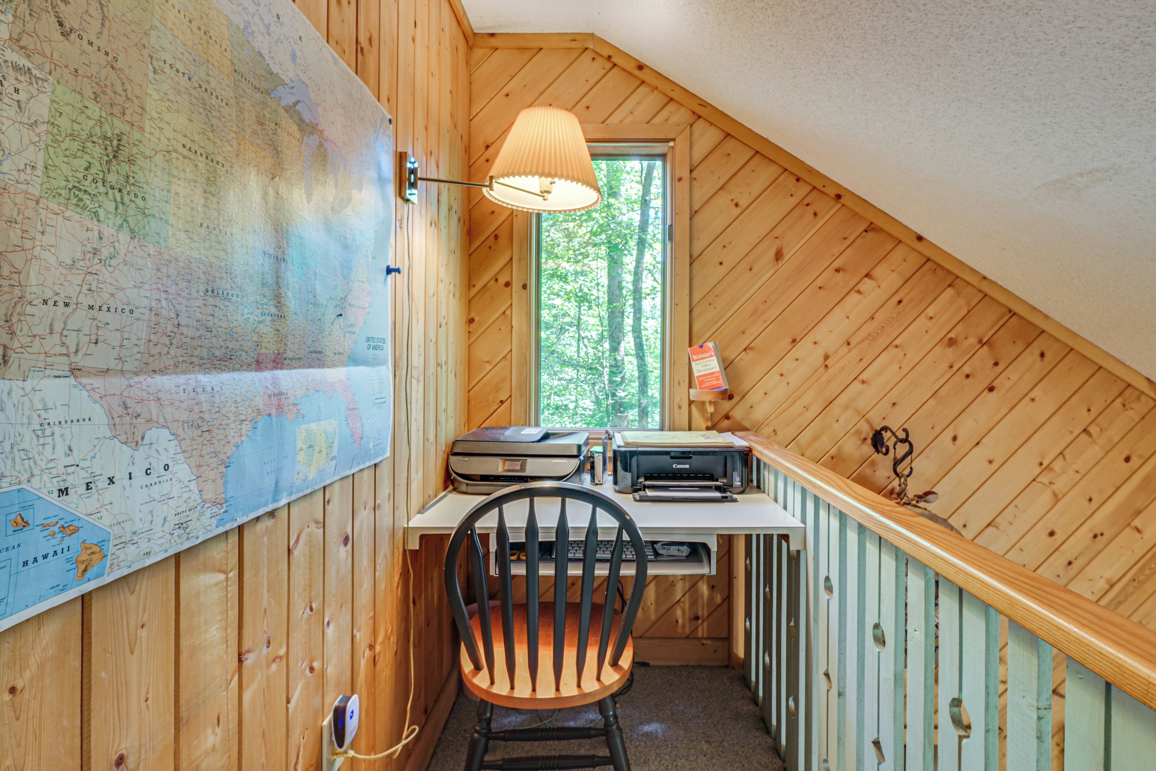 A wooden interior with a desk, chair, map, printer, and lamp.