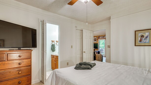 A bedroom with a bed, a wooden dresser, a television, and a door leading to another room.