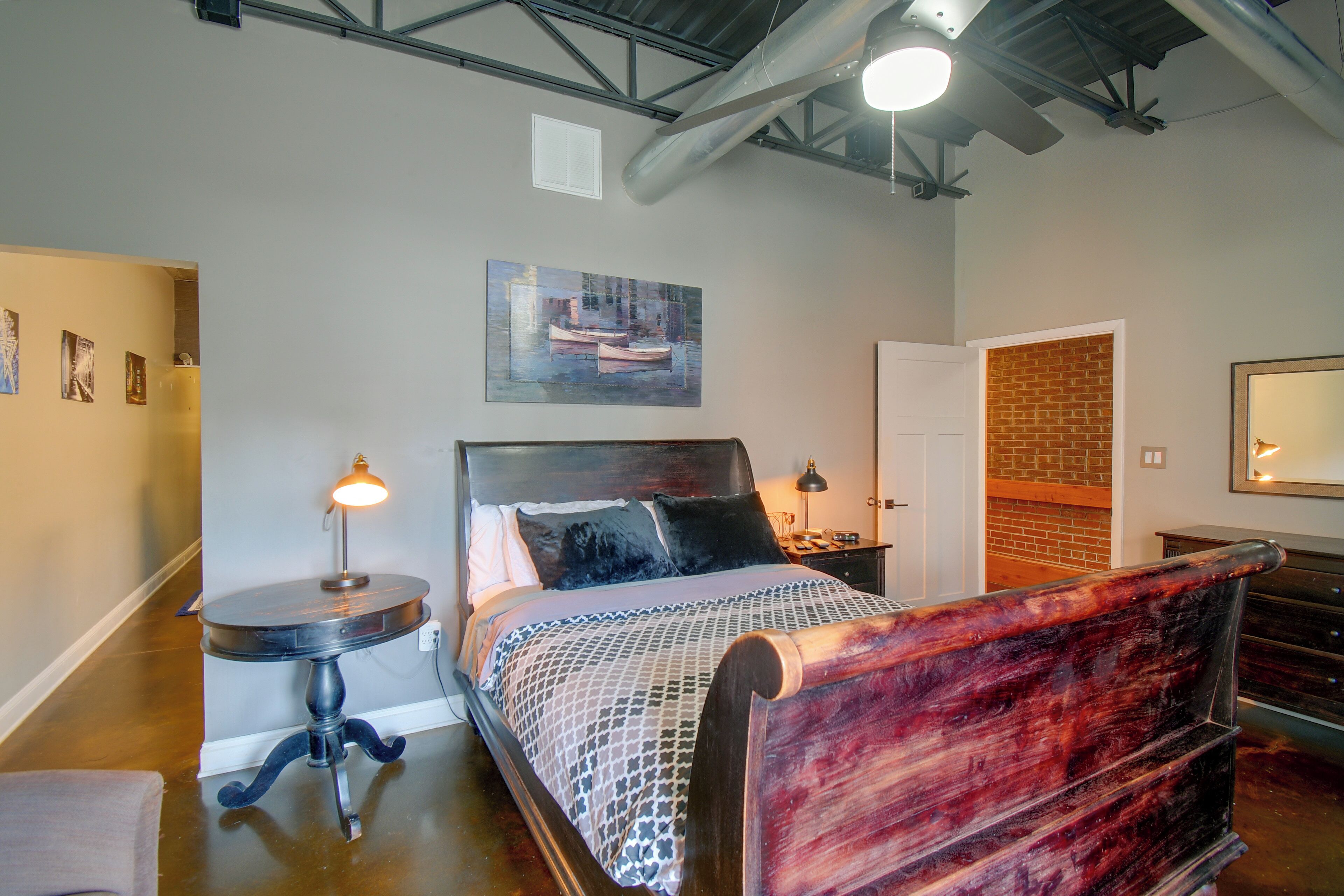 A bedroom with a bed, bedside table, lamp, and a painting on the wall.