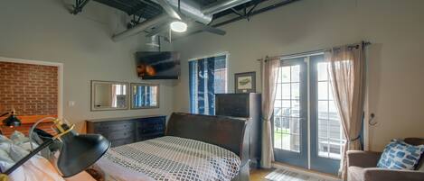 Un dormitorio con cama, cómoda, televisor y ventana con cortinas.