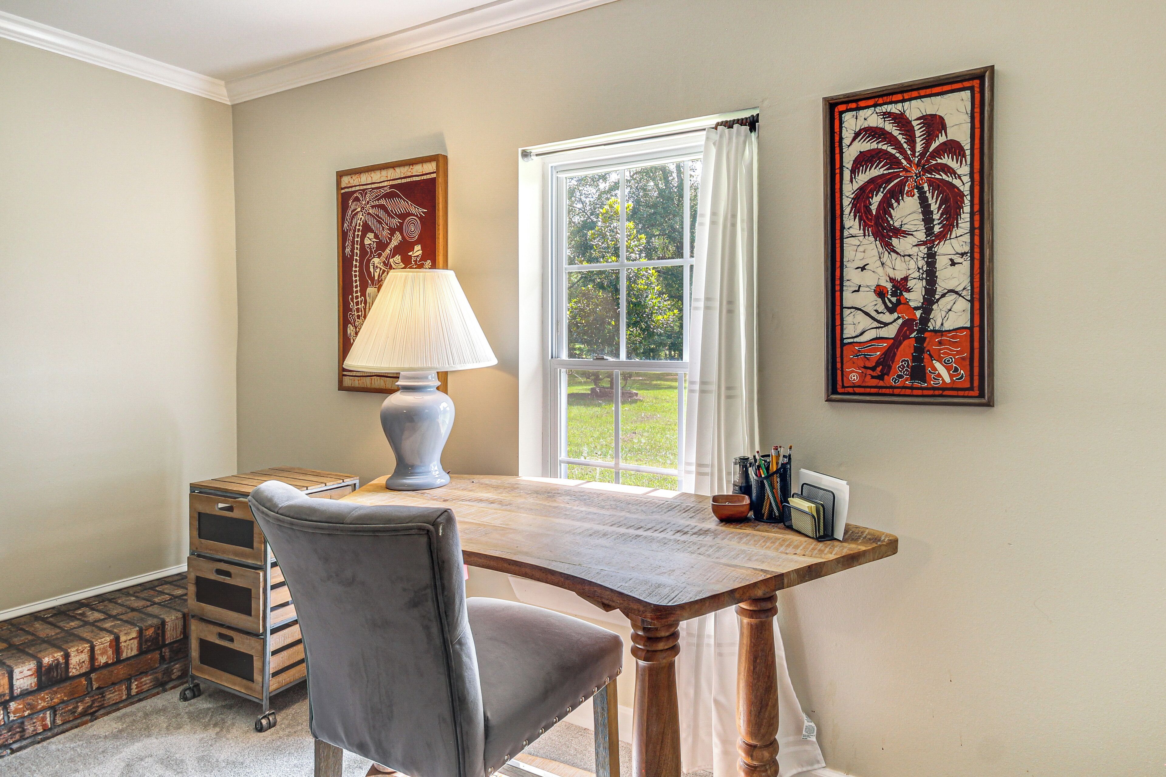 A room with a wooden desk, a grey chair, a lamp, and two framed artworks on the wall.