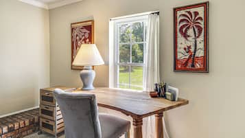 Une pièce avec un bureau en bois, une chaise grise, une lampe et deux œuvres d’art encadrées accrochées au mur.