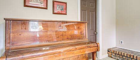 Un piano en bois se trouve dans une pièce dotée d’une porte et de deux tableaux encadrés accrochés au mur.