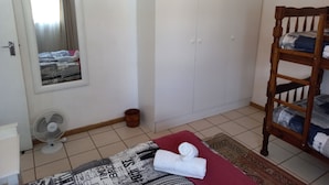 Un dormitorio con cama, armario, espejo, ventilador y una silla de madera.