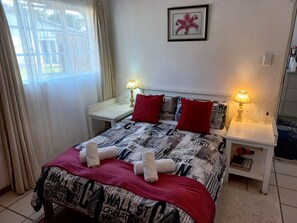 A neatly made bed with a patterned bedspread, two red pillows, and two white towels folded on top. There are two bedside tables with lamps, a framed picture on the wall, and a window with curtains. - The Heidelberger (Heidelberg)