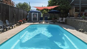 A rectangular swimming pool with a clear blue water surface, surrounded by a concrete deck. There are lounge chairs and a small shed with a red canopy in the background. - Private Pool & Basketball Spacious 3BR Sleeps 9 (Wenatchee)