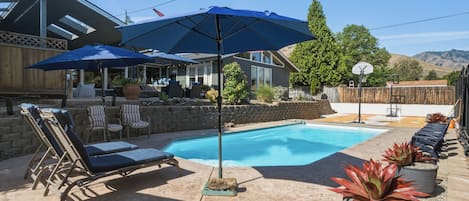 A backyard with a swimming pool, lounge chairs, and a basketball hoop.
