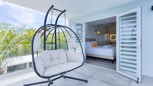 Ein Balkon mit einer Hängematte, ein Bett mit weißer Bettwäsche und Blick auf Palmen.