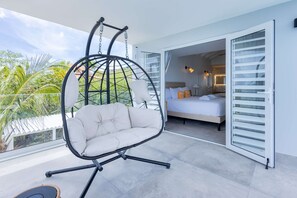 Ein Balkon mit einer Hängematte, ein Bett mit weißer Bettwäsche und Blick auf Palmen.