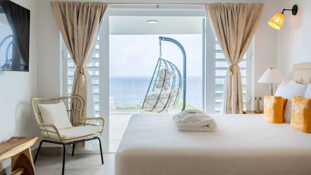 Ein Hotelzimmer mit Bett, Stuhl, Hängesessel und Blick aufs Meer.