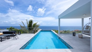 Ein Infinity-Pool auf dem Dach mit Blick aufs Meer, Gartenmöbel und eine überdachte Lounge-Ecke.