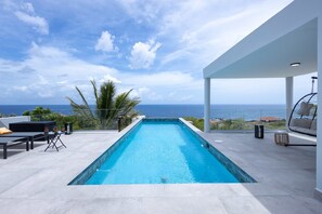 Ein Infinity-Pool auf dem Dach mit Blick aufs Meer, Gartenmöbel und eine überdachte Lounge-Ecke.