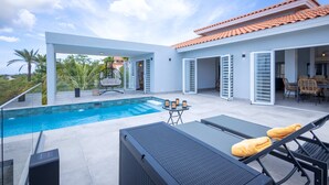 Ein moderner Poolbereich im Freien mit freiem Blick zum Himmel, ein Essbereich mit Stühlen und eine überdachte Terrasse mit Tisch und Stühlen.
