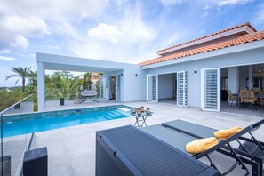 Ein moderner Poolbereich im Freien mit freiem Blick zum Himmel, ein Essbereich mit Stühlen und eine überdachte Terrasse mit Tisch und Stühlen.