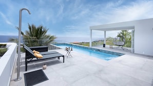 A rooftop pool area with a view of the ocean, a lounge chair, a table with lanterns, and a hanging chair.