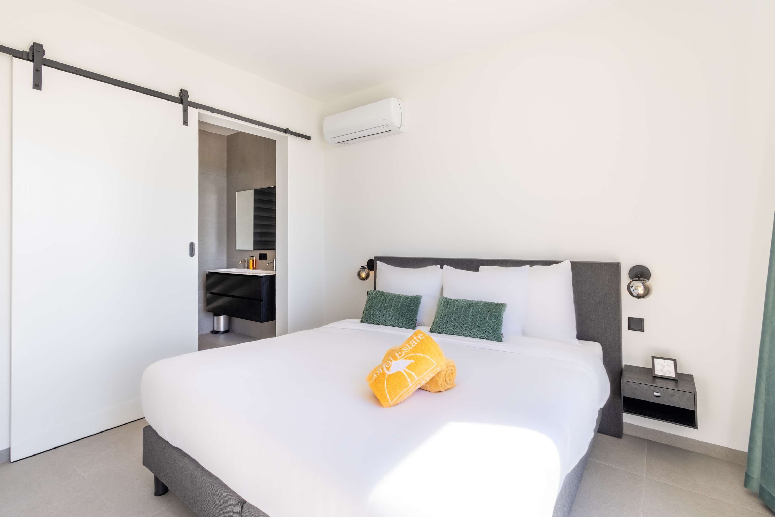 Quarto de hotel com cama, mesa de cabeceira, escrivaninha e guarda-roupa.