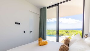 Une chambre d’hôtel moderne dotée d’un grand lit, offrant une vue sur une piscine et sur la verdure, et munie d’une porte-fenêtre coulissante.