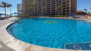 A hotel with a swimming pool, palm trees, and a clear blue sky. - Wake Up to the Sea Oceanfront Retreat W207 (Puerto Peñasco)