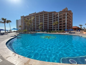 A hotel with a swimming pool, palm trees, and a clear blue sky. - Wake Up to the Sea Oceanfront Retreat W207 (Puerto Peñasco)